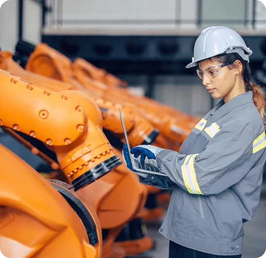 Profissional utilizando um notebook diante de robôs industriais